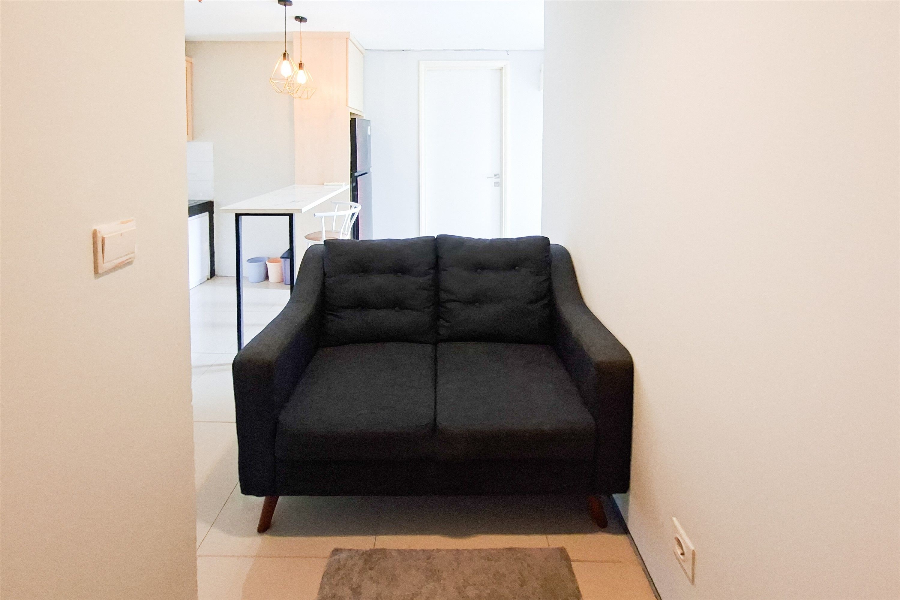 A black sofa in a living area with a white door and a kitchen in the background.
