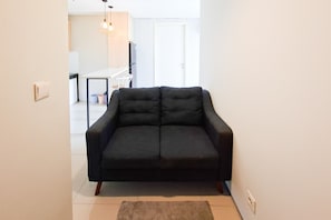 Un sofá negro en una sala de estar con una puerta blanca y una cocina al fondo.