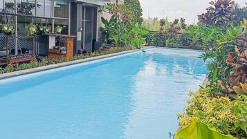 A swimming pool with a sign for a live food stall, surrounded by lush greenery and a modern building in the background.