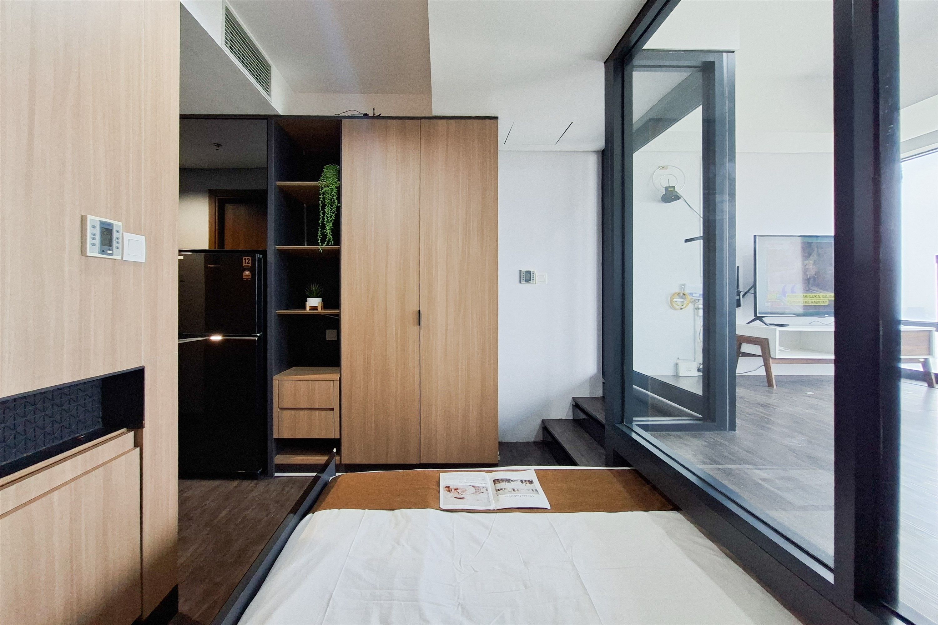 A modern bedroom with a large window, a bed, a wardrobe, and a small plant.