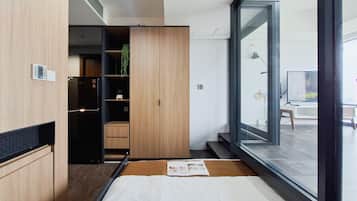 A modern bedroom with a large window, a bed, a wardrobe, and a small plant.