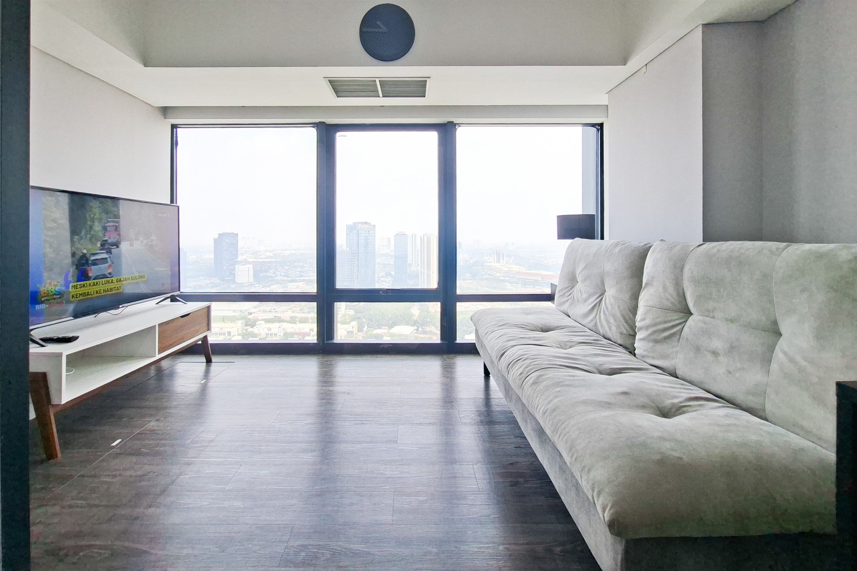 Una sala de estar moderna con un ventanal grande, un sofá, un televisor y piso de madera.