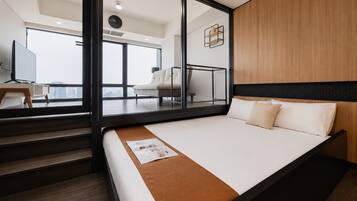 Una habitación de hotel moderna con una cama grande, cabecera de madera, separador de vidrio y vistas a la ciudad.