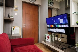 Ein modernes Wohnzimmer mit einem roten Sofa, einem Fernseher, der einen Homescreen anzeigt, und einer Holztür.