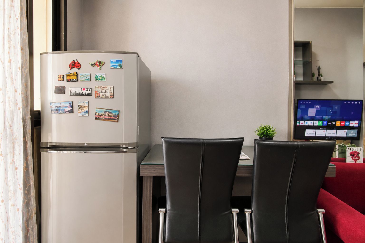 A compact kitchen with a refrigerator, two chairs, a dining table, and a television.