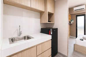 Eine kleine Küche mit Spüle aus Edelstahl, Holzschränken und einem schwarzen Kühlschrank.