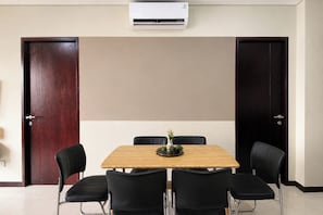 A conference room with a wooden table, four black chairs, a small plant on the table, and an air conditioning unit above. - Homey And Roomy 3Br At Apartment Nifarro Park (Jakarta)