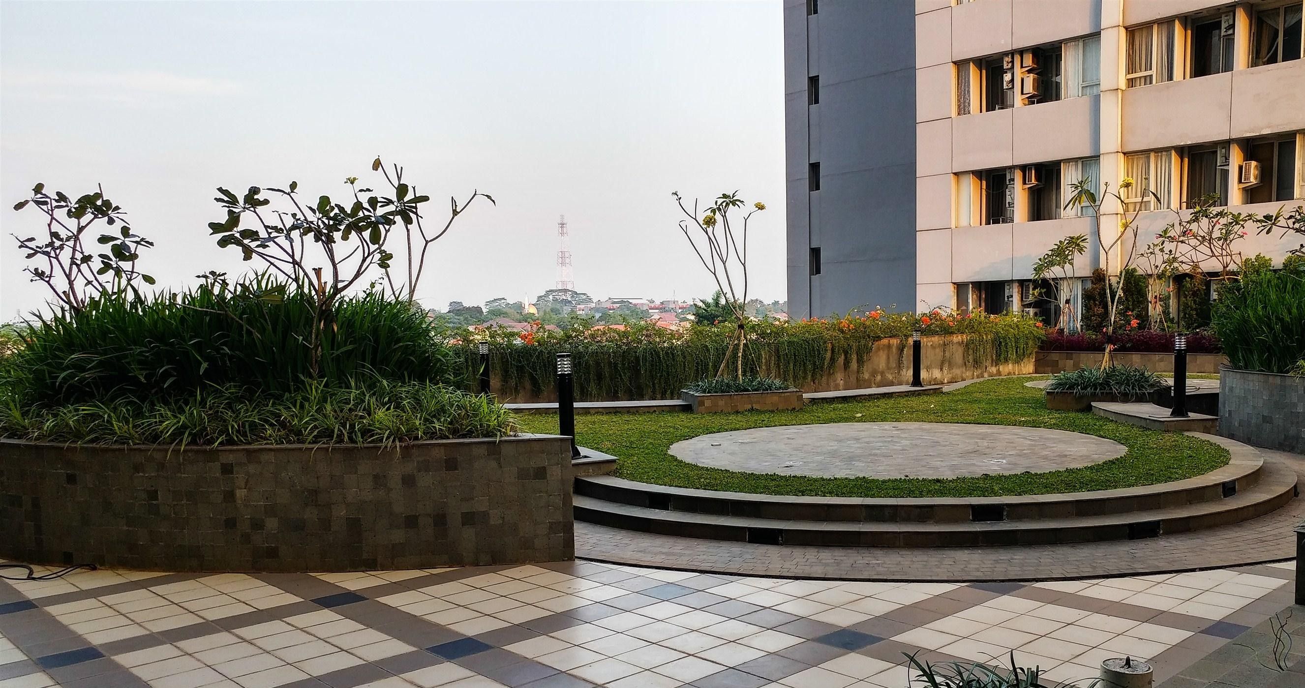 A courtyard with a circular garden, a tiled floor, and a building in the background.