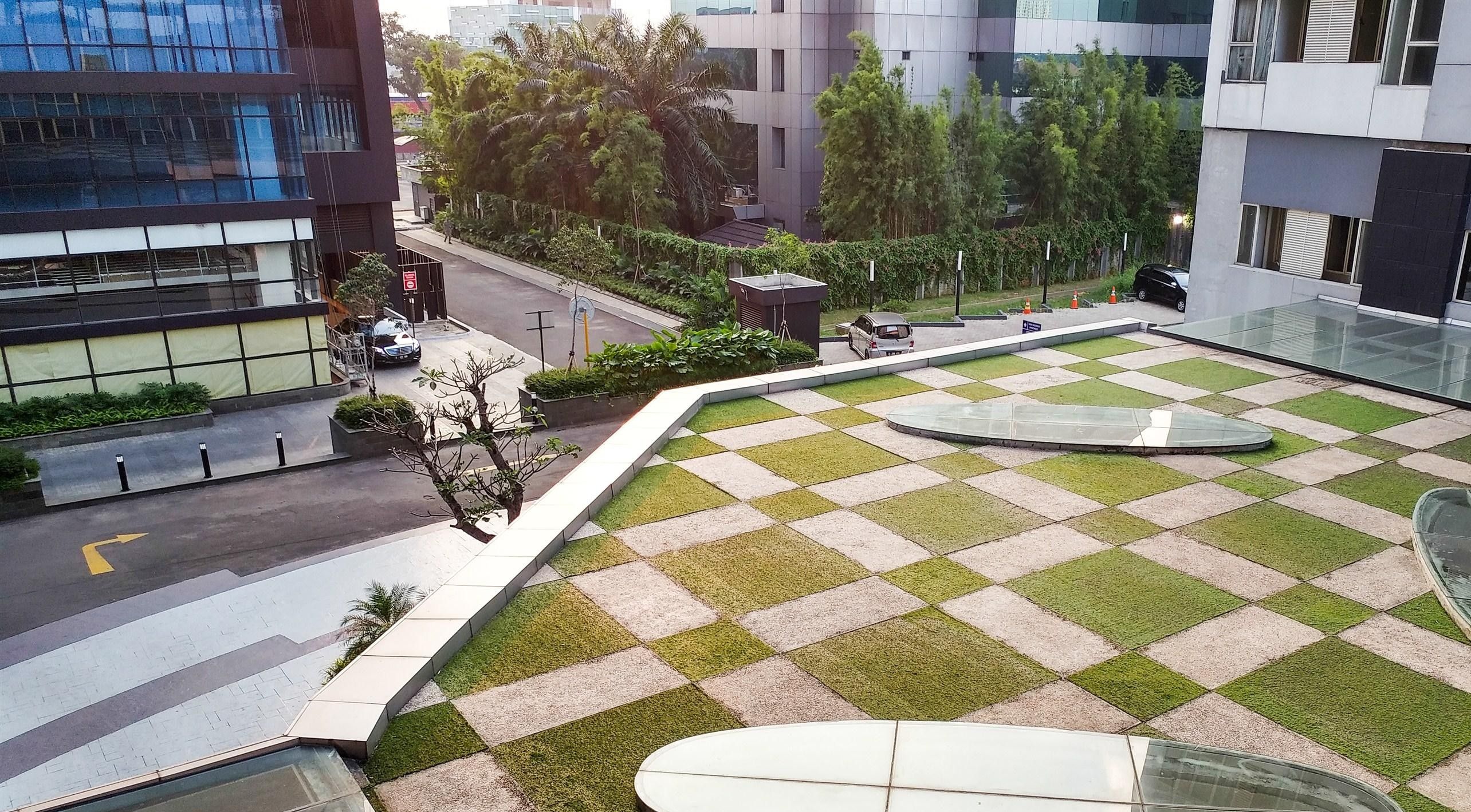 A courtyard with a checkered pattern of grass and paving, surrounded by modern buildings.