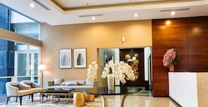 A modern hotel lobby with a sofa, chairs, a coffee table, and decorative elements like orchids and framed pictures. - Homey And Roomy 3Br At Apartment Nifarro Park (Jakarta)