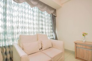 A room with a beige sofa, a wooden cabinet, and a window with sheer curtains. - Stylish Designed Studio At Apartment Grand Kamala Lagoon (Bekasi)