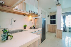 A modern kitchen with a stainless steel sink, a stove, and a refrigerator. - Stylish Designed Studio At Apartment Grand Kamala Lagoon (Bekasi)