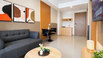 A modern living room with a grey sofa, a round coffee table with decorative items, a TV mounted on the wall, and a kitchen area in the background.