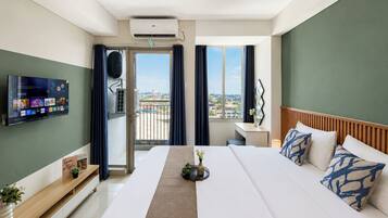 Habitación de hotel con una cama, un televisor montado en la pared, un ventanal con cortinas y un balcón con vistas.