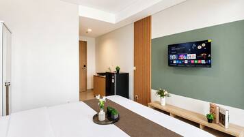 Habitación de hotel con una cama grande, un escritorio, un televisor de pantalla plana montado en la pared y una pequeña kitchenette al fondo.