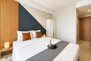 Quarto de hotel com cama, mesa de cabeceira, abajur e uma planta sobre a cama.