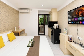 A hotel room with a bed, a desk, a television, a kitchenette, and a view of greenery. - Lovely And Cozy Studio At Apartment Kebagusan City (Jakarta)