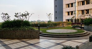 A rooftop garden with a circular seating area, surrounded by planters with various plants, and a view of a cityscape in the background. - Tastefully Designed 3Br At Apartment Nifarro Park (Jakarta)