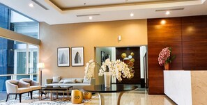 A modern lobby with a sofa, chairs, a coffee table, and decorative elements like orchids and framed pictures. - Tastefully Designed 3Br At Apartment Nifarro Park (Jakarta)