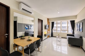 Une chambre d’hôtel moderne avec une table à manger en bois, des chaises noires, un canapé, un téléviseur et une grande fenêtre avec des rideaux.