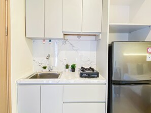 A kitchen with white cabinets, a stainless steel sink, a gas stove, and a refrigerator. - Strategic Location Studio Room At Apartment Meikarta District 2 (Cikarang)