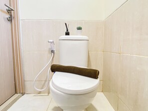 A white toilet with a brown seat cover, a white flush handle, and a small potted plant on top of the tank. - Strategic Location Studio Room At Apartment Meikarta District 2 (Cikarang)