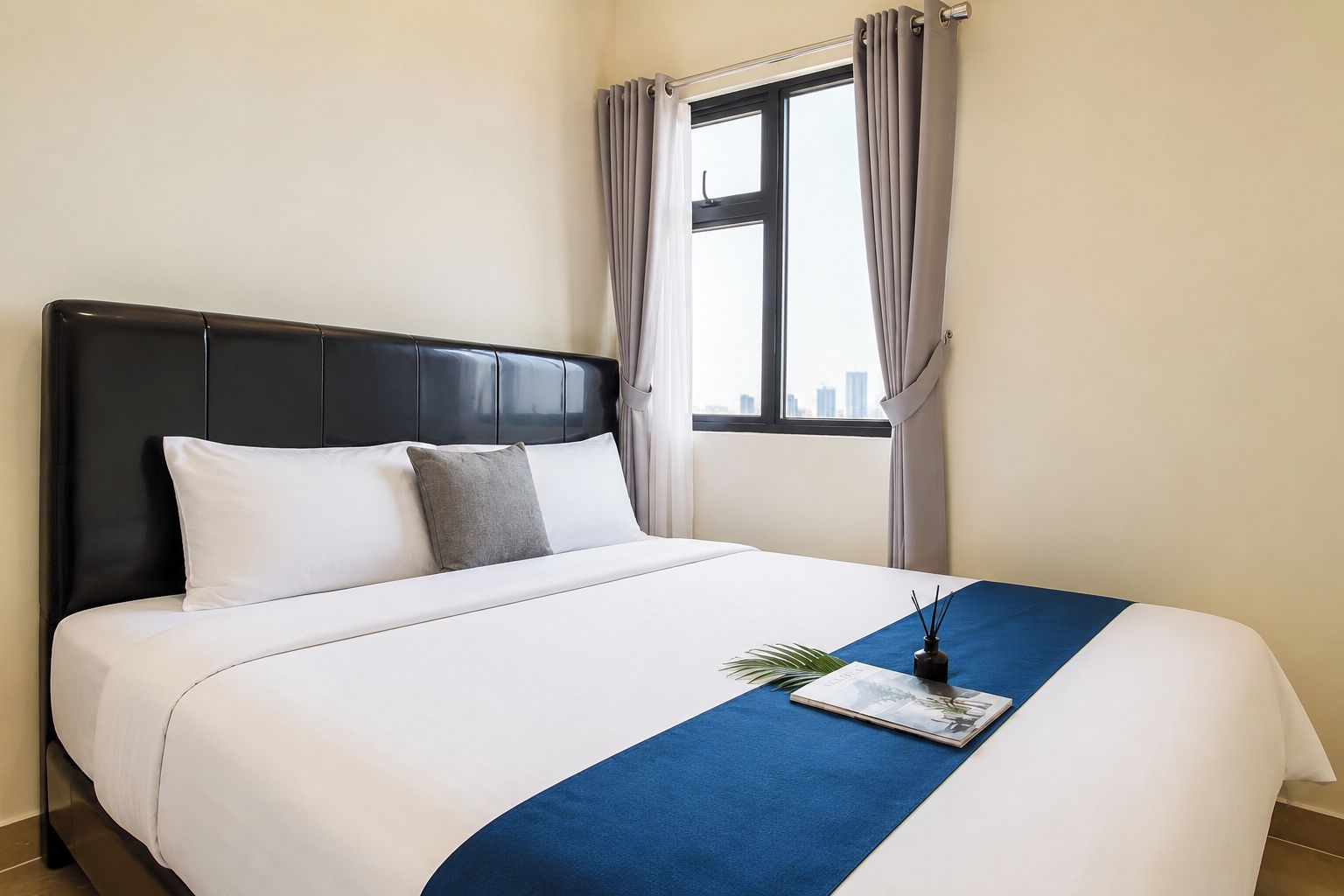 A hotel room with a bed, a window with curtains, and a blue accent on the bedspread.