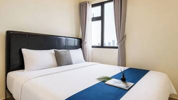 A hotel room with a bed, a window with curtains, and a blue accent on the bedspread.