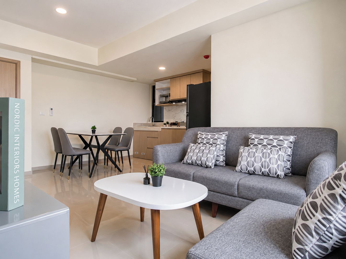 A modern living room with a grey sofa, a white coffee table, and a dining area with chairs and a table.