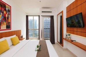 A hotel room with a bed, a TV, a window with curtains, and a city view. - Modern And Homey Studio At Apartment Ciputra World 2 (Jakarta)