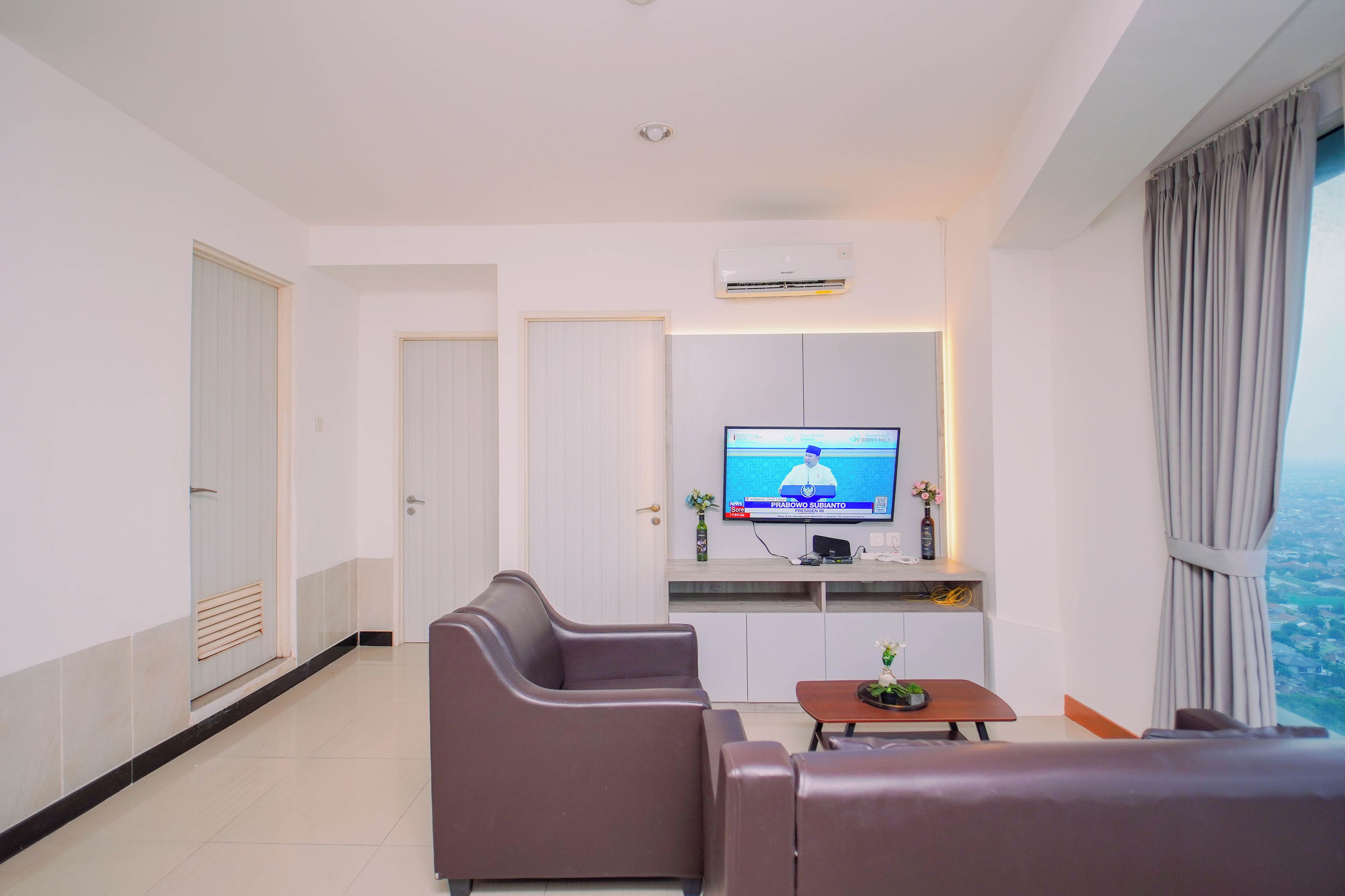 Una sala de estar moderna con televisor de pantalla plana, un sofá, una mesa de centro y vista a la ciudad.