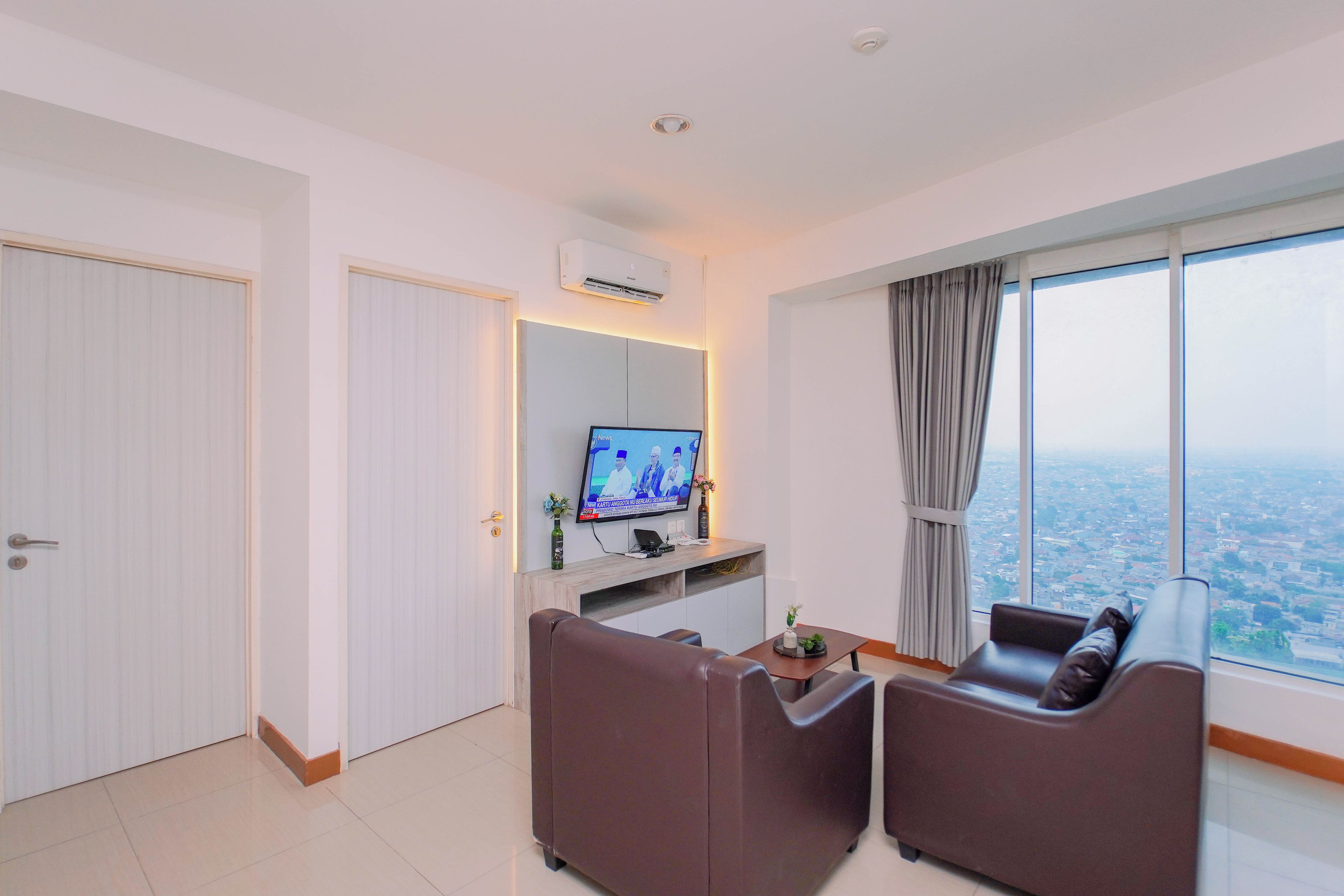 A modern living room with a television, seating area, and a large window offering a city view.