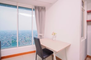 A room with a large window, a table, a chair, and a vase with flowers. - Relaxing 2Br With City Lights At Apartment Grand Kamala Lagoon (Bekasi)