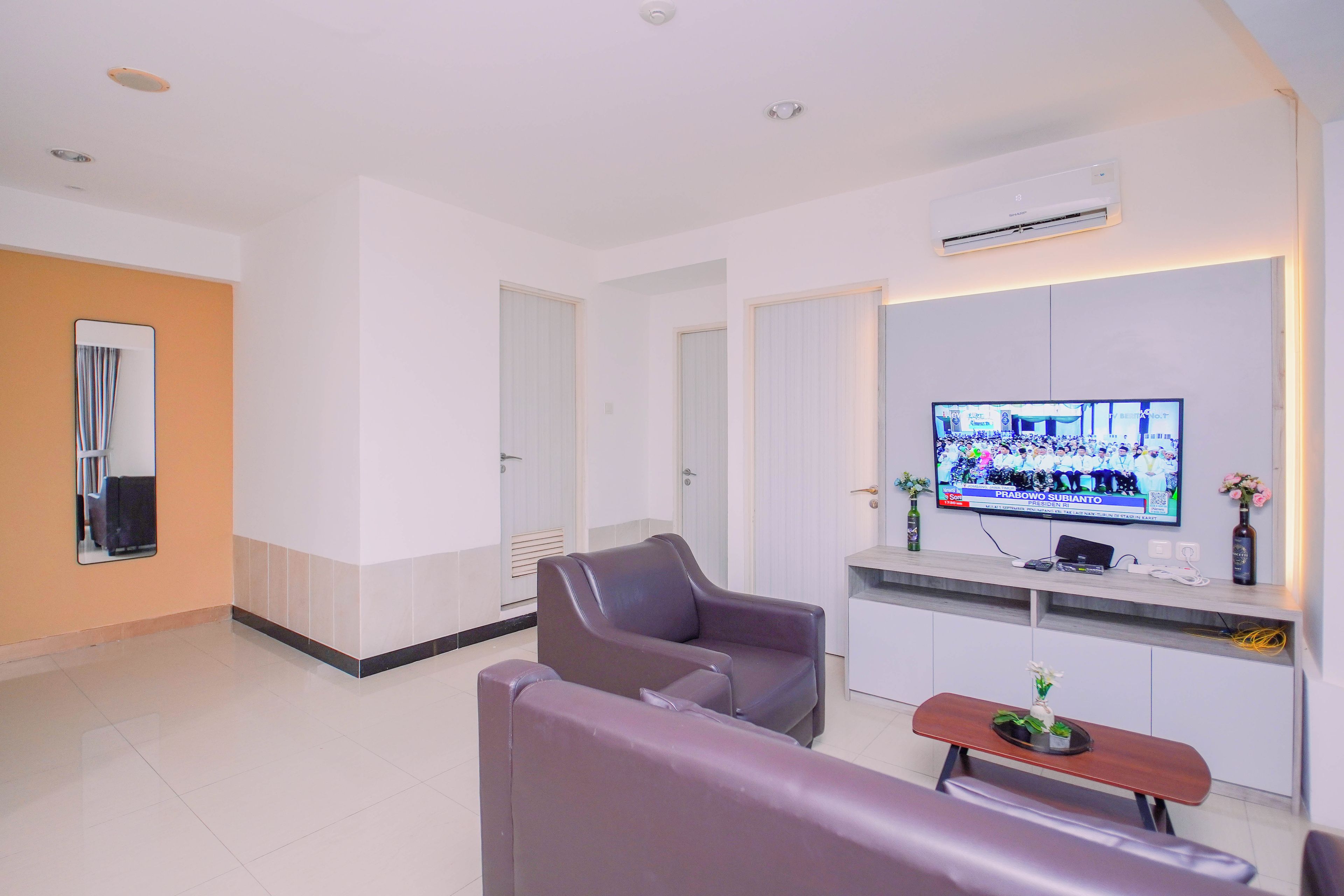 A modern living room with a flat-screen TV, a sofa, a coffee table, and a small decorative plant.