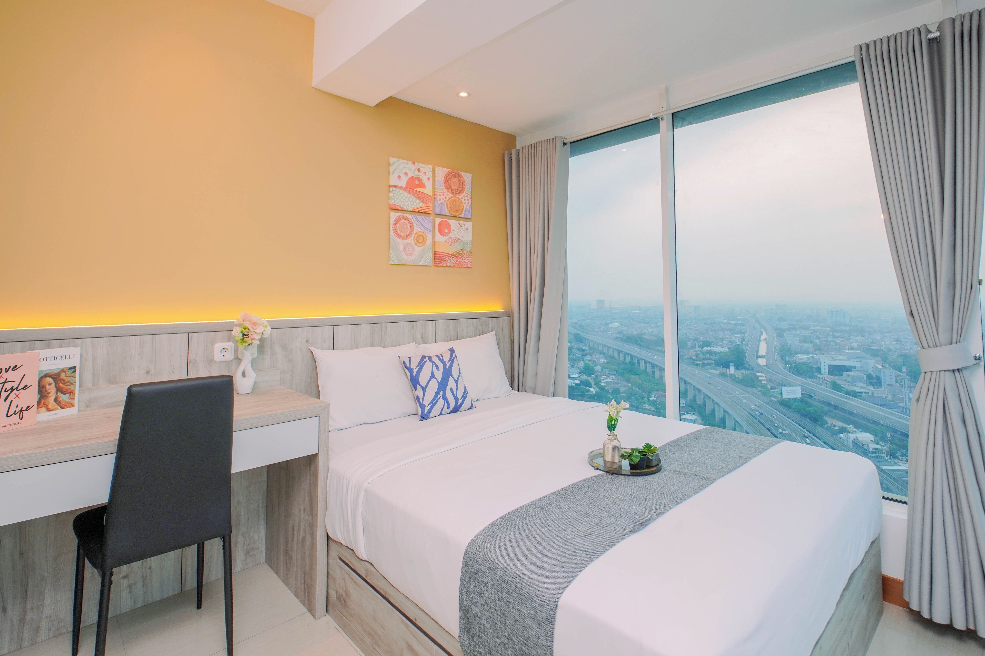Habitación de hotel con una cama grande, un escritorio y vistas a un paisaje urbano a través de un ventanal amplio.