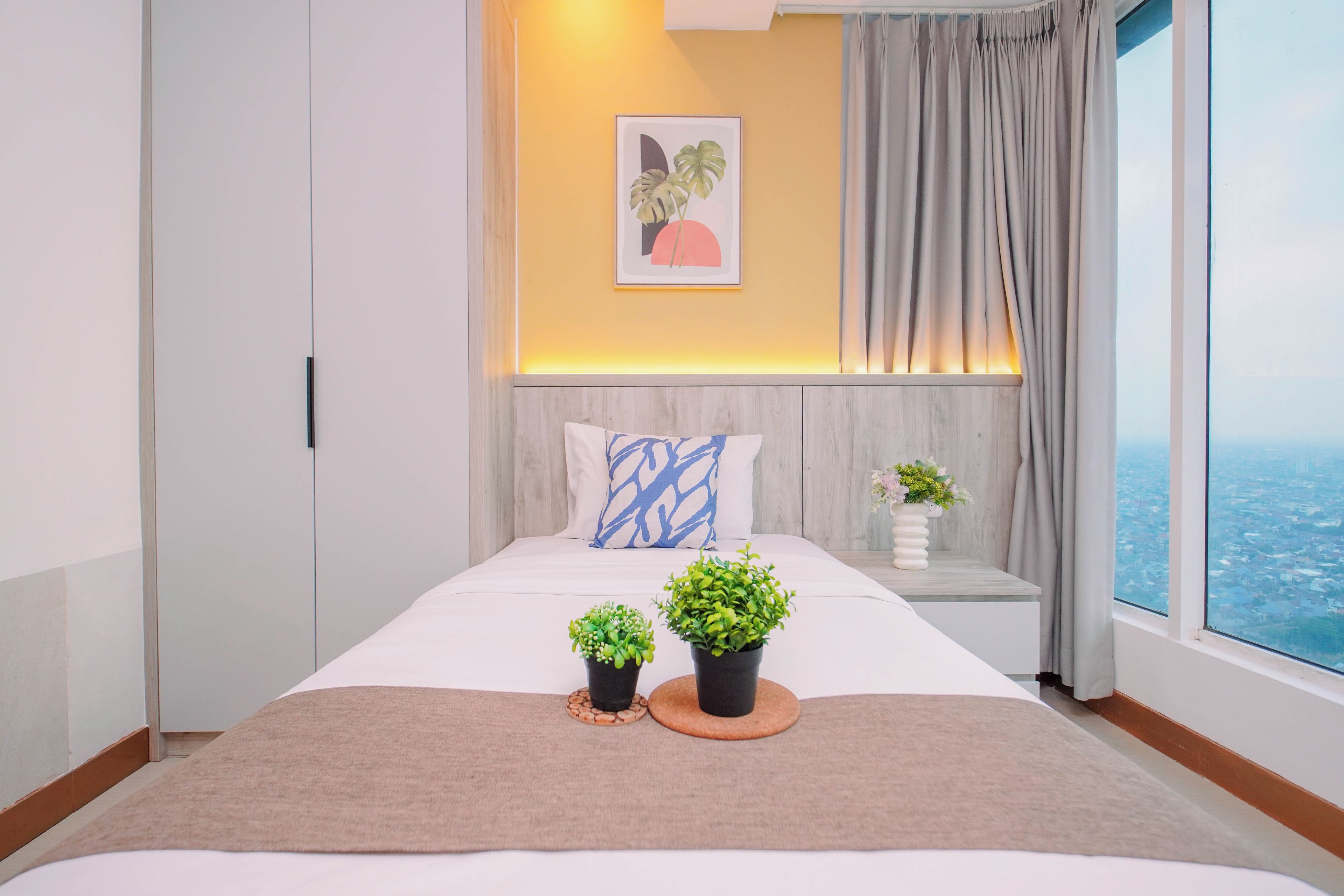 A modern bedroom with a large bed, a headboard, a bedside table with a plant, and a city view through the window.