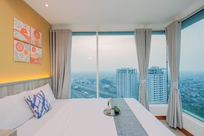 A hotel room with a large bed, a view of the cityscape, and a window with curtains. - Relaxing 2Br With City Lights At Apartment Grand Kamala Lagoon (Bekasi)