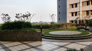 A landscaped courtyard with a circular seating area, a tiled floor, and a building with multiple windows. - Capacious And Comfortable 3Br At Apartment Nifarro Park (Jakarta)
