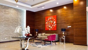 A modern living room with a sofa, a red chair, a coffee table, a lamp, and a painting on the wall. - Capacious And Comfortable 3Br At Apartment Nifarro Park (Jakarta)