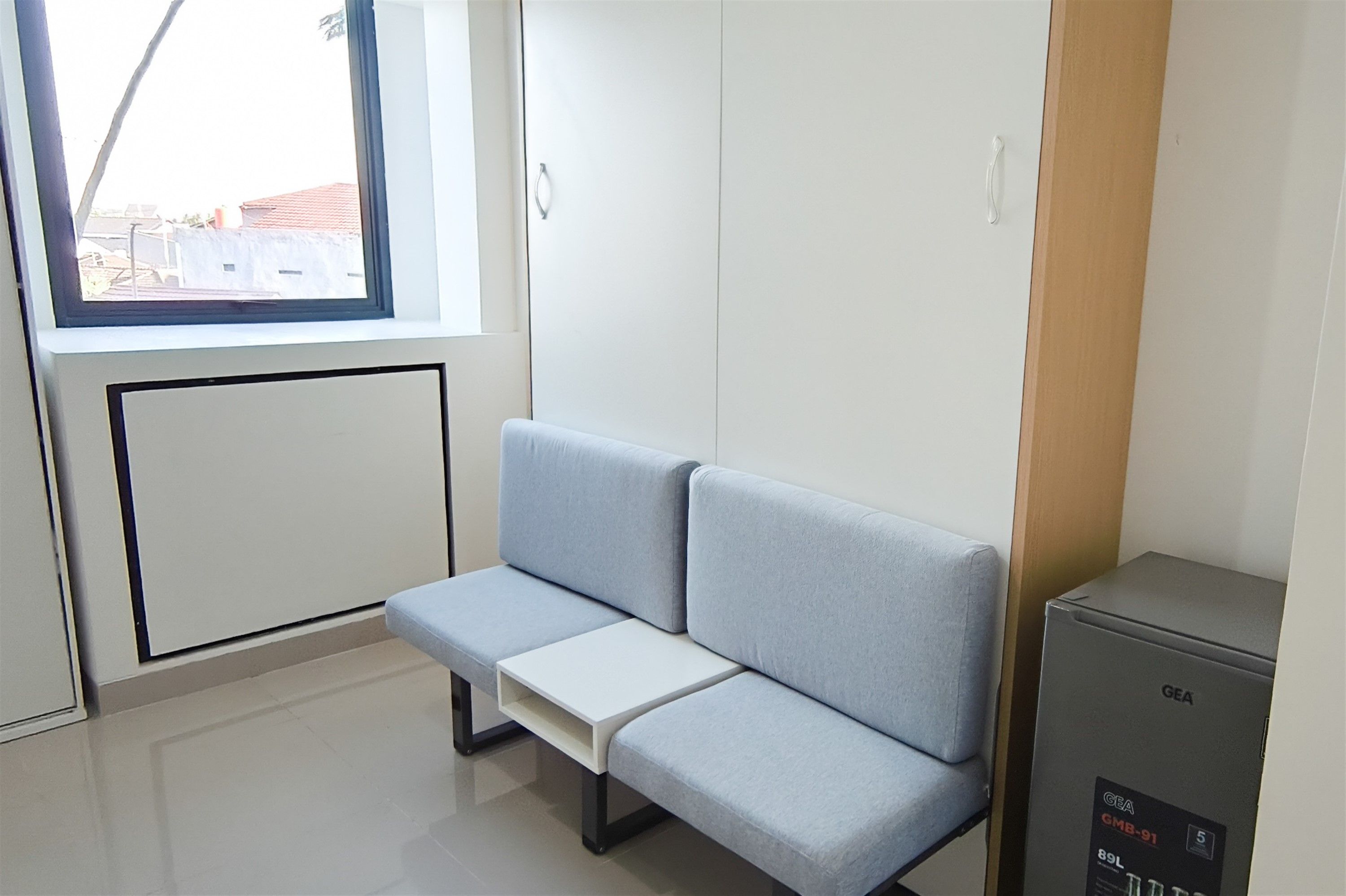 Ein Zimmer mit einer grauen Couch, einem kleinen Tisch und einem GEA-Gerät.