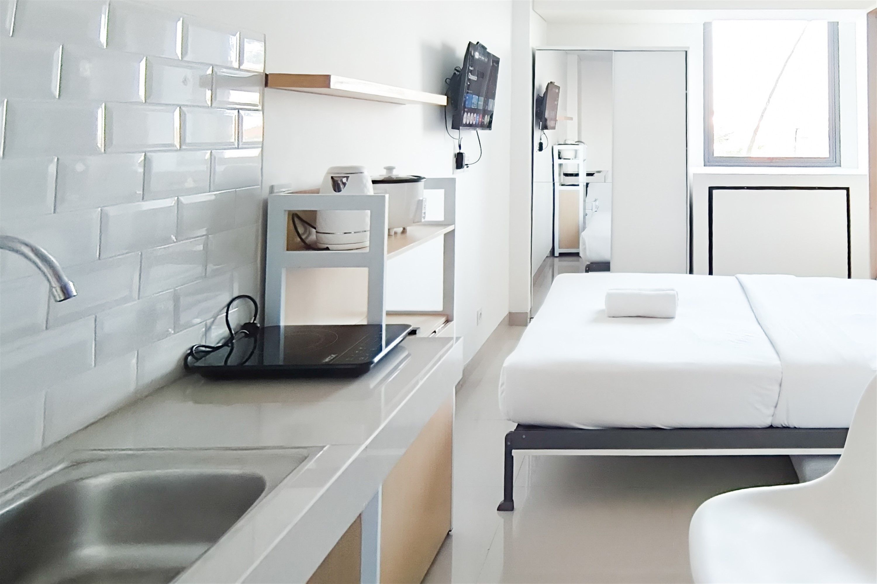 Habitació d'hotel moderna amb cuina americana, un llit i un bany visibles al fons.