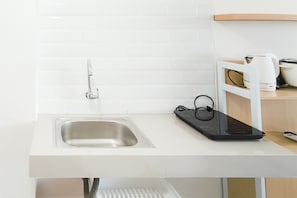 A kitchen with a stainless steel sink, a white countertop, and a black electronic device. - Bright Studio Room At Apartment Bandaraya - Tallasa City Makassar (Makassar)