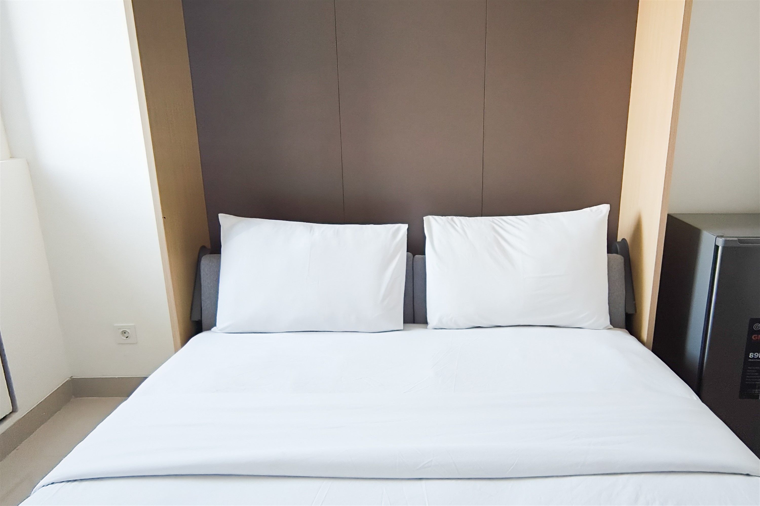 A hotel room with a large bed, two pillows, a headboard, and a small desk with a computer.