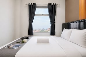 A hotel room with a bed, a window with curtains, a view of the city, and a magazine on the nightstand. - Good Deal Spacious 2Br At Apartment Grand Asia Afrika (Bandung)