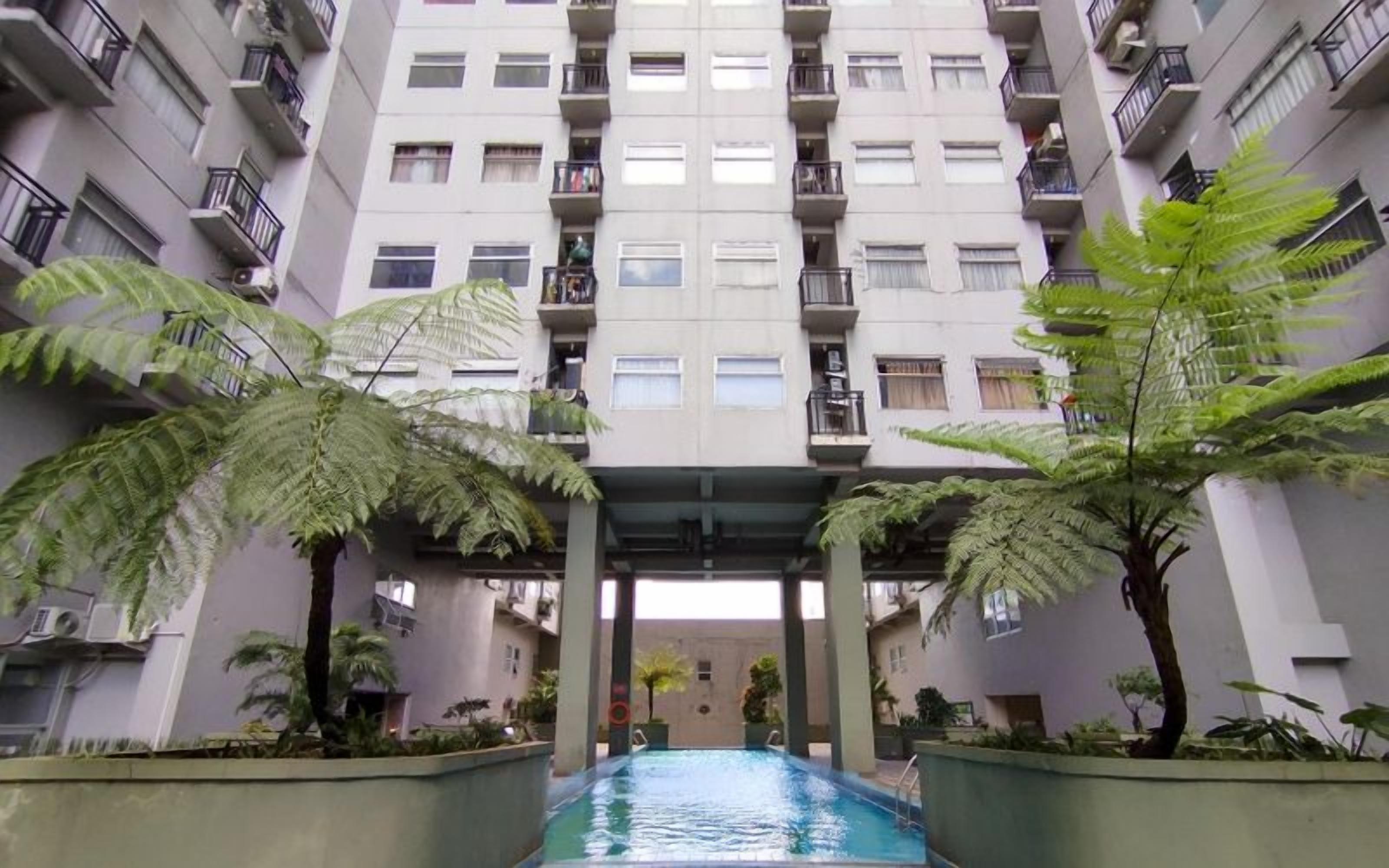 A multi-story residential building with a central courtyard featuring a swimming pool, surrounded by potted plants and ferns.