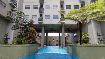 A swimming pool with a tiled edge, surrounded by greenery and a multi-story building with balconies.