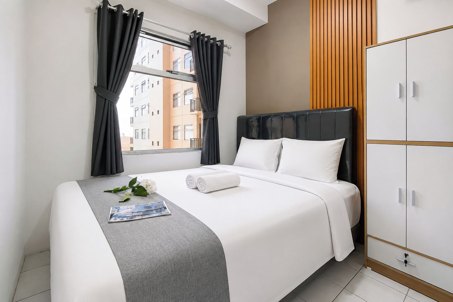 A hotel room with a bed, a wardrobe, a window with curtains, and a view of buildings outside.