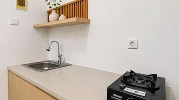 A kitchen with a sink, faucet, countertop, wooden cabinets, a shelf with decorative items, and a portable gas stove.