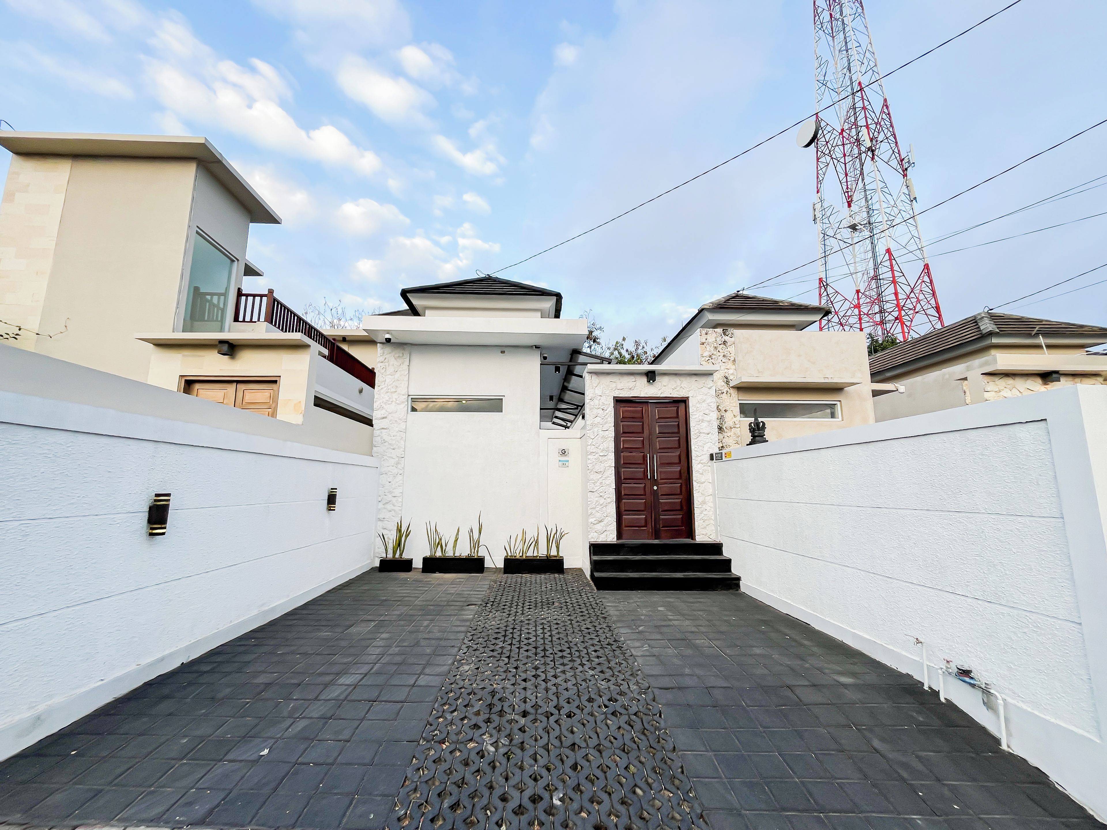 A modern residential building with a central entrance, a staircase leading to the entrance, and a tall communication tower in the background.