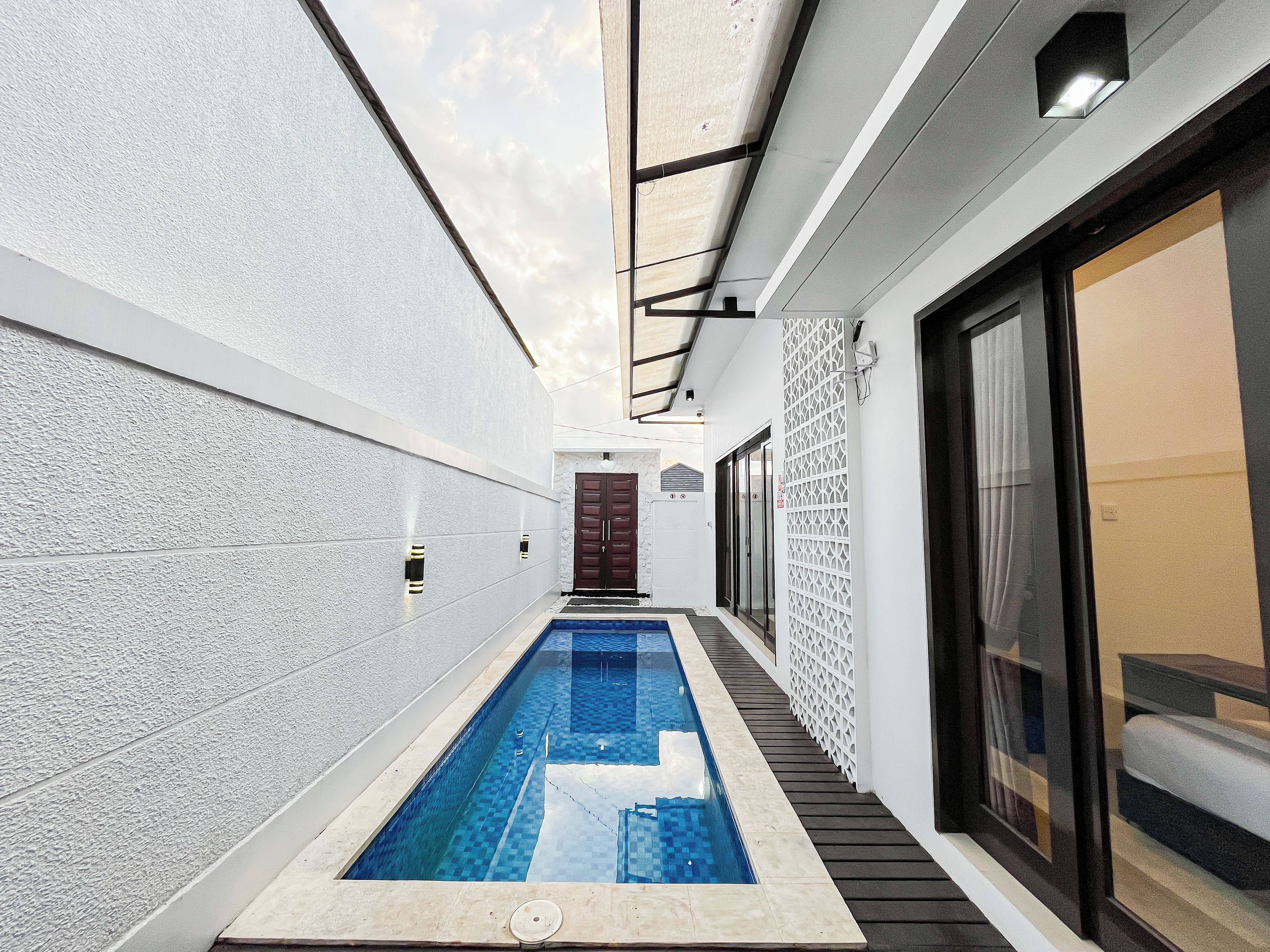 A narrow indoor swimming pool with a tiled floor, flanked by white walls and a wooden deck.